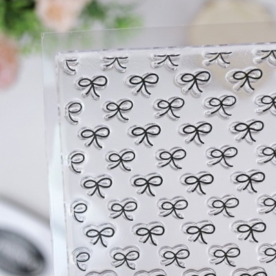 Placa transparente com padrão repetido de laços em relevo.
