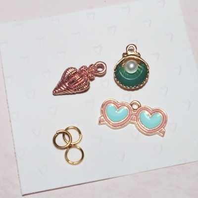 Conjunto de pendentes coloridos com argolas douradas sobre cartão branco com padrão de corações