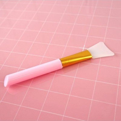 Pincel aplicador rosa com ponta de silicone transparente sobre superfície rosa quadriculada