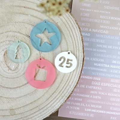 Pendentes festivos azuis, rosa e branco com formas recortadas sobre superfície branca texturada, com folha rosa com texto em espanhol ao lado.