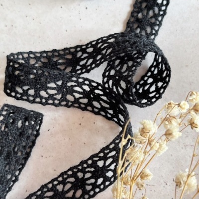 Fita de renda preta com padrão aberto e ramos secos ao lado