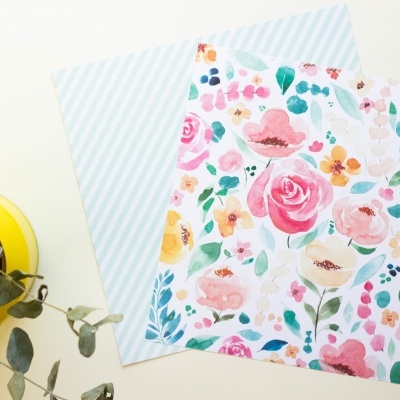 Lenços de tecido com padrões floral e de listras azuis ao lado de vaso amarelo com plantas.