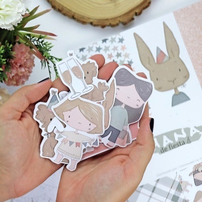 Recortes de papel com desenhos de crianças em tons pastel nas mãos sobre mesa com decoração