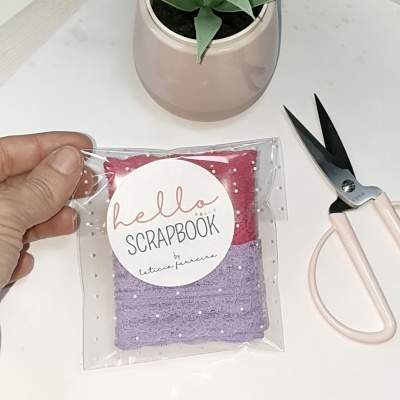 Tecidos decorativos rosados em embalagem plástica transparente, tesoura rosa e planta em vaso rosa claro