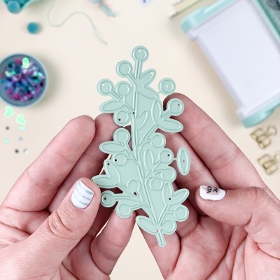 Mãos segurando carimbo de silicone verde claro com padrão de folhas e bagas