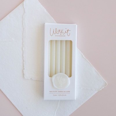 Embalagem branca com cinco velas de cera visíveis e texto em cima, sobre papel branco texturizado e fundo rosa claro