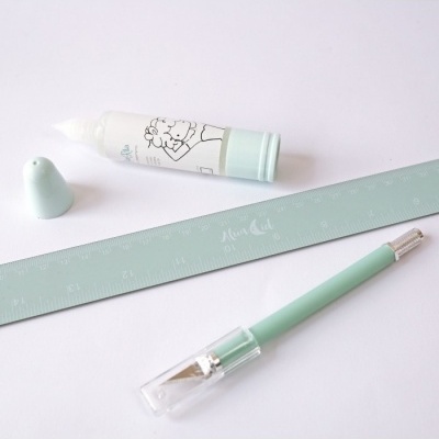 Tubo de cola branca, régua azul clara e caneta azul clara sobre superfície branca