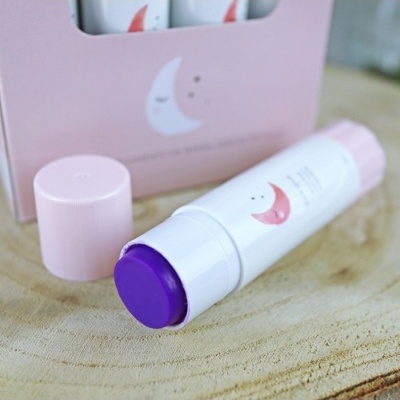 Bálsamo em stick com tampa rosa e corpo branco com desenho de lua, sobre madeira