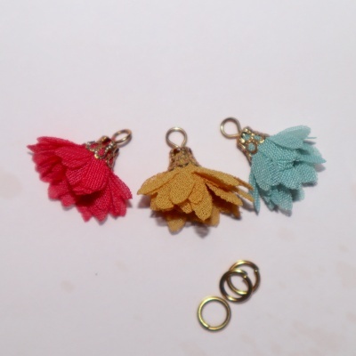 Três pendentes flor em tecido vermelho, amarelo e azul com argolas metálicas douradas num fundo branco