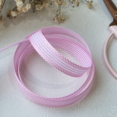 Fita decorativa rosa e branca com bordas recortadas sobre superfície branca com flores secas e tesoura rosa