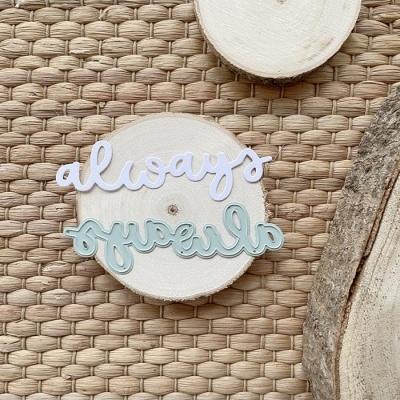 Placa decorativa com a palavra 'always' em branco e azul claro sobre disco de madeira natural em tapete trançado