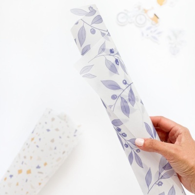 Rolo de papel decorativo com padrão de folhas cinza segurado por mão feminina