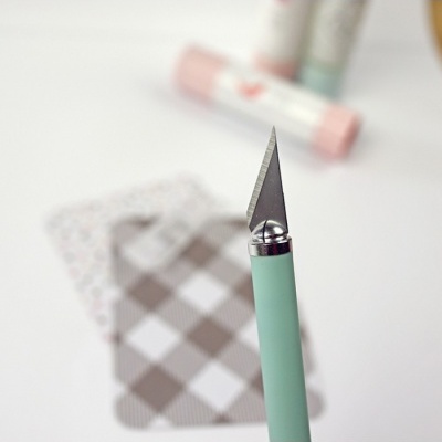 Faca de corte com lâmina triangular e cabo verde pastel em fundo com cartões e cola