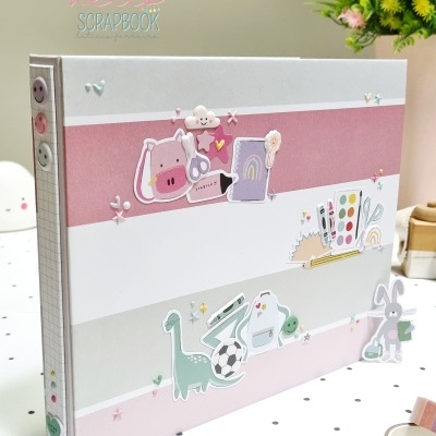 Álbum scrapbook com faixas coloridas e adesivos decorativos sobre mesa com toalha pontilhada