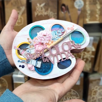 Paleta de pintura decorativa com tinta azul, flor rosa, pincel e texto em madeira