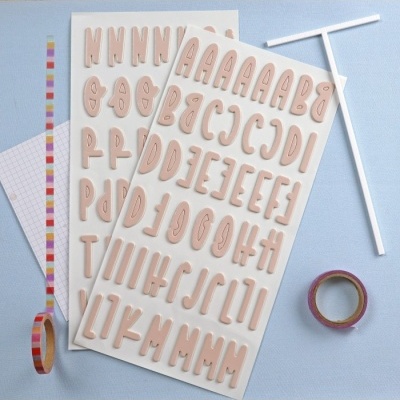 Autocolantes de letras maiúsculas bege em folhas com fita adesiva colorida e papel quadriculado