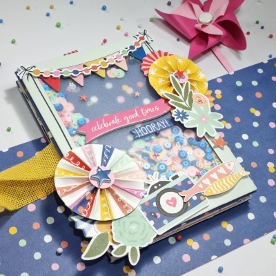 Caixa decorativa colorida com confetes e elementos festivos sobre tecido azul com bolinhas