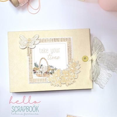 Álbum de scrapbook decorado com flores e borboleta em bege com fita de renda, tesoura rosa, cartão e rolos de fio