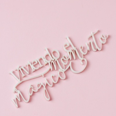 Palavra decorativa branca com texto em espanhol sobre fundo rosa.