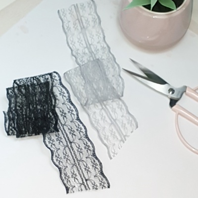 Fitas de renda preta e branca com tesoura e vaso com planta