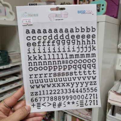 Autocolantes de letras, números e símbolos em preto numa embalagem de cartão branco com etiquetas e textos visíveis.