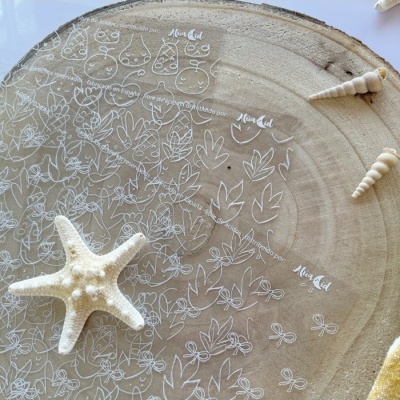 Placa transparente redonda com desenhos brancos sobre madeira com estrela do mar e conchas