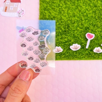 mão segura adesivo transparente com flores pretas e rosas contra tapete verde e mesa rosa