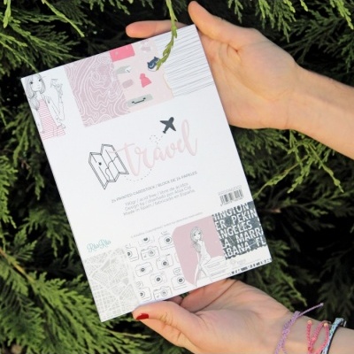 Caderno de viagem com capa decorada em tons pastel segurado por mãos femininas