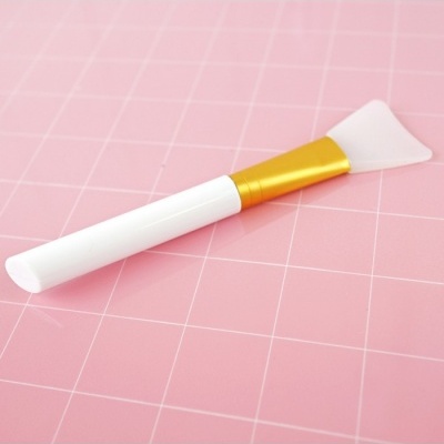 Pincel aplicador branco com detalhe dourado numa superfície rosa quadriculada