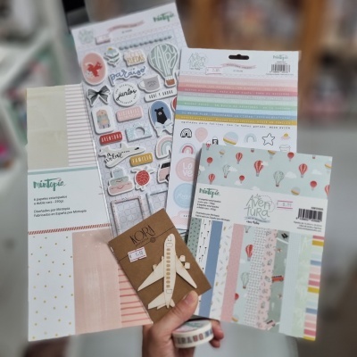 Materiais para scrapbooking com papéis estampados, autocolantes e um avião em madeira.