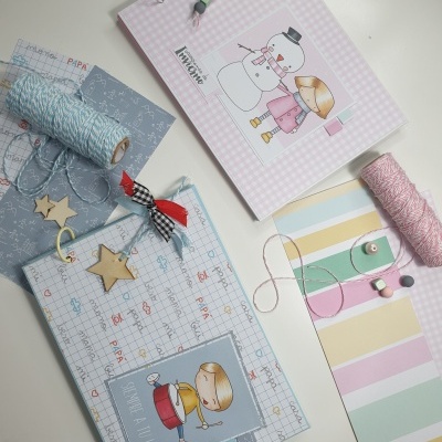 Dois álbuns infantis decorados com desenhos de boneco de neve e menina, e menina loira, sobre mesa com rolos de fio e papel decorativo