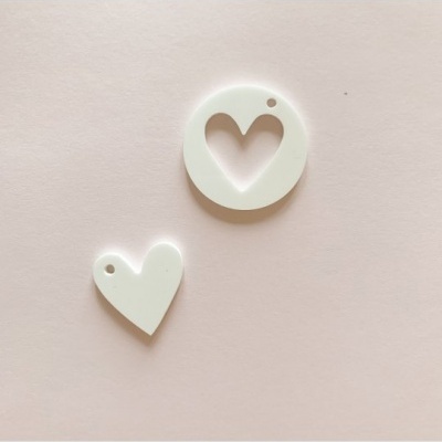 Dois pendentes brancos em forma de coração e círculo com coração recortado, fundo rosa claro.