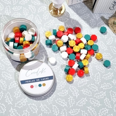 frascos de pérolas de lacre coloridas sobre toalha cinza com padrão de folhas brancas