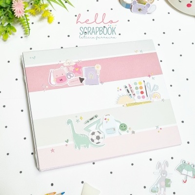 Caderno de scrapbook colorido com ilustrações infantis sobre superfície branca com pontos pretos e materiais de arte