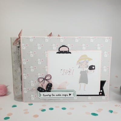 Álbum de fotografia cinza com padrão floral e ilustração de menina com câmera, texto 2021 e frase curtro la vida aqui.