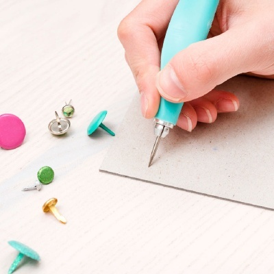 ferramenta de gravação azul claro com tachinhas coloridas em mesa branca