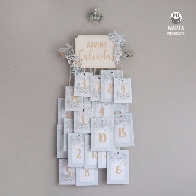 Calendário de advento branco e azul com números dourados pendurado na parede cinza