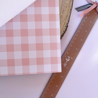 Caixa xadrez rosa e branco ao lado de régua transparente e fita decorativa