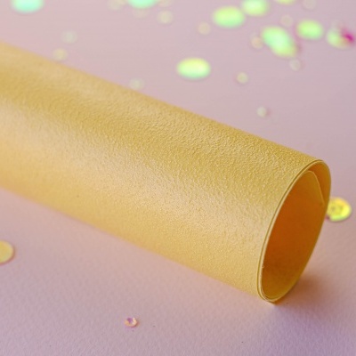 Papel texturizado amarelo enrolado sobre fundo rosa com confetes coloridos.