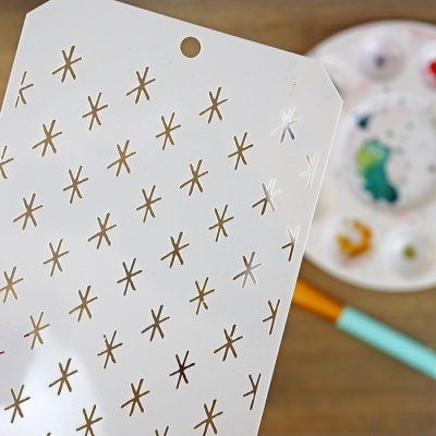 Folha branca com padrões dourados e prateados, paleta de pintura e pincel ao fundo