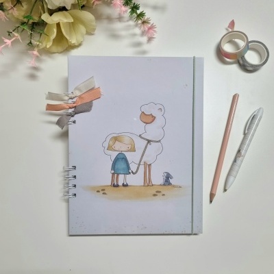 Caderno ilustrado com menina, ovelha e rato e acessórios de escrita ao lado