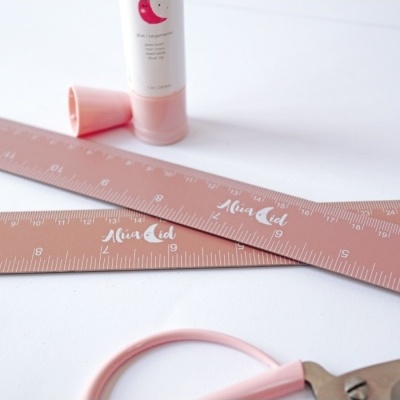 Dois réguas cor-de-rosa AlivaAid, tubo de creme cor-de-rosa e ferramenta com cabo cor-de-rosa sobre fundo branco