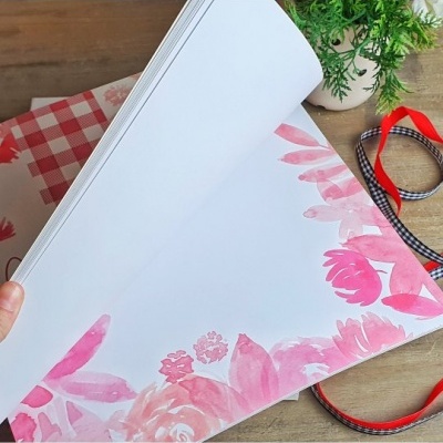 Bloco de folhas decoradas com flores cor de rosa em mesa de madeira com fitas e planta