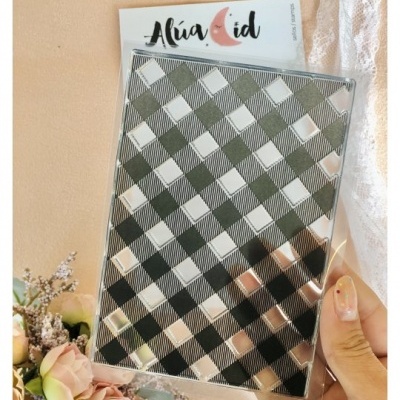 Caderno com capa xadrez preto e branco em plástico transparente, etiqueta Alúa Cid, flores ao lado