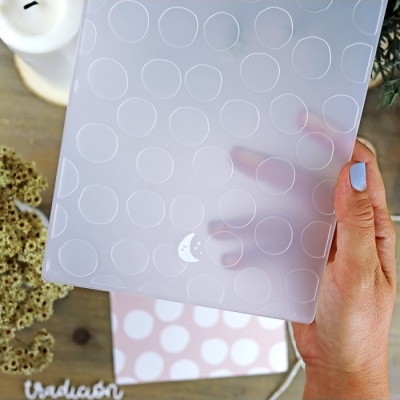 Capa transparente fosca com padrão de círculos e meia-lua branca, mão segurando sobre mesa com vela e plantas