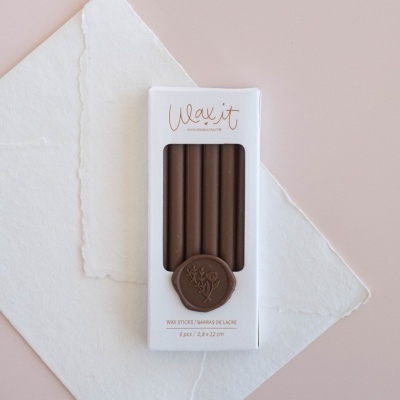 Caixa branca com 5 varetas de lacre marrons e selo decorativo, sobre papel texturizado