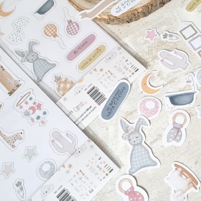 Duas folhas de autocolantes coloridos com desenhos de animais, balões e formas em tons pastel numa superfície clara