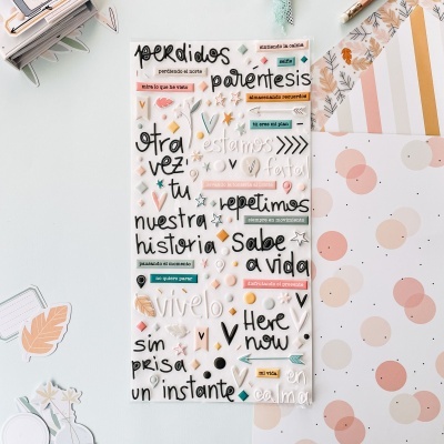 Folha translúcida com adesivos de palavras e frases em espanhol sobre mesa clara com folhas decoradas em tons pastel