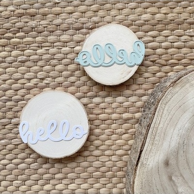 Ornamentos de madeira redondos com a palavra 'hello' em azul claro e branco sobre superfície texturada