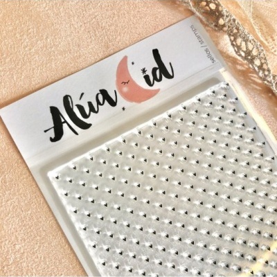 Folha de autocolantes transparentes com brilhos prateados em embalagem com etiqueta 'Alúa Cid' em superfície bege